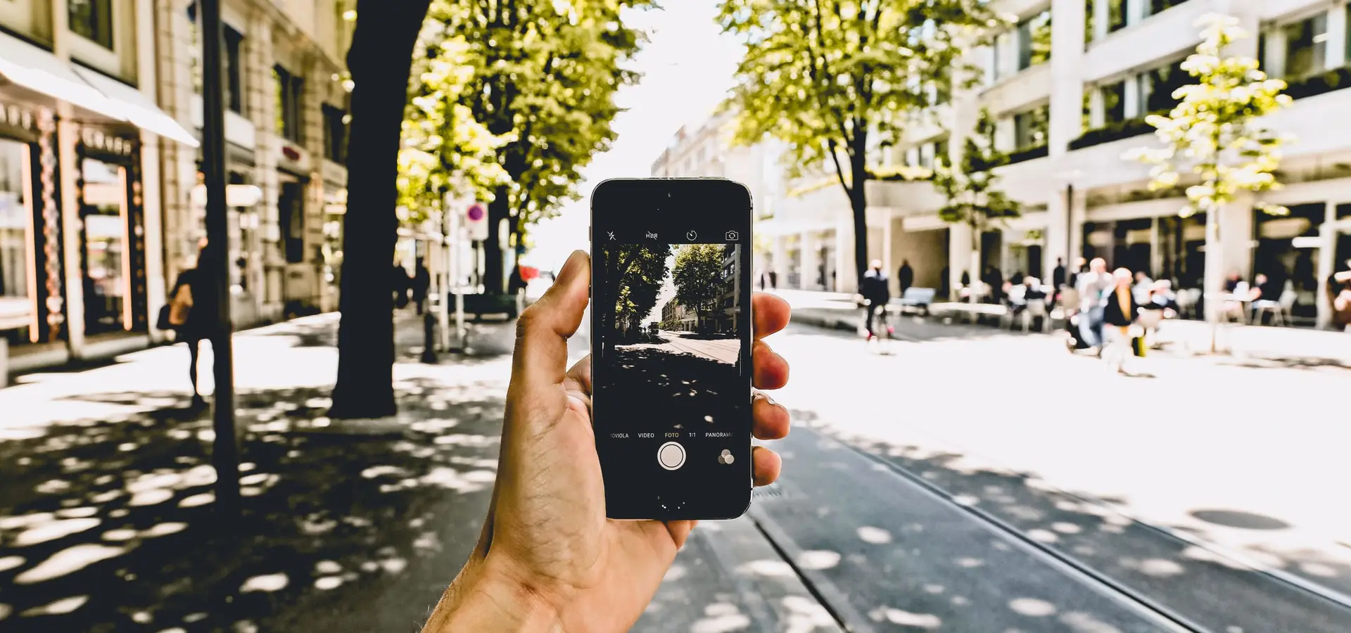 Hand mit Smartphone in einer sonnigen Straße